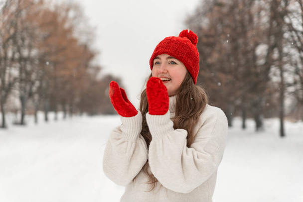 Сміється щаслива дівчина в червоному капелюсі і рукавицях в зимовому парку. Красива молода жінка на зимовій ходьбі
. - Фото, зображення
