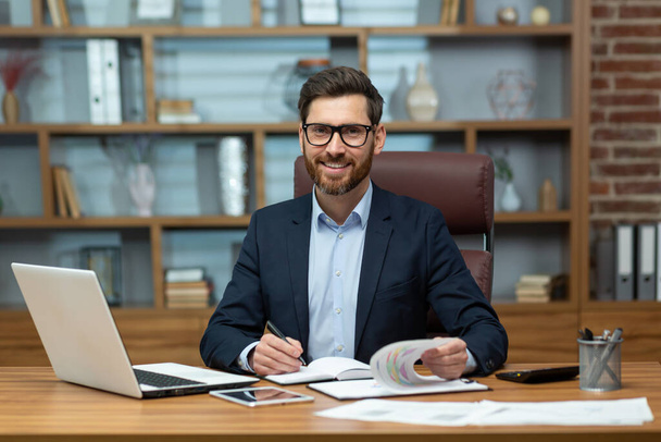 Portrait of successful and happy mature financier, senior businessman with beard and glasses smiling and looking at camera, man working inside office on paper work, investor satisfied with result. - Foto, imagen