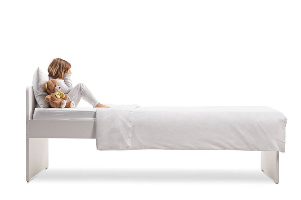 Chica triste en pijama sentada en una cama y llorando aislada sobre fondo blanco - Foto, imagen