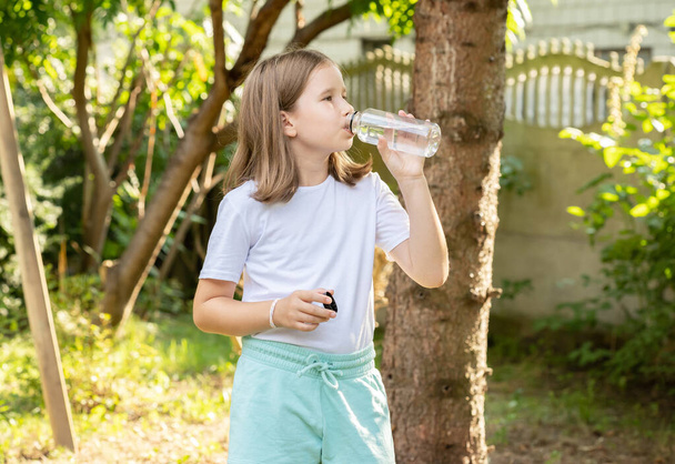 Спортивный ребенок школьного возраста, девушка, пьющая свежую фильтрованную воду из многоразовой пластиковой бутылки на открытом воздухе, копировальное пространство, вид сбоку, размытый фон, один человек, крупный план Гидрация, освежающая концепция - Фото, изображение