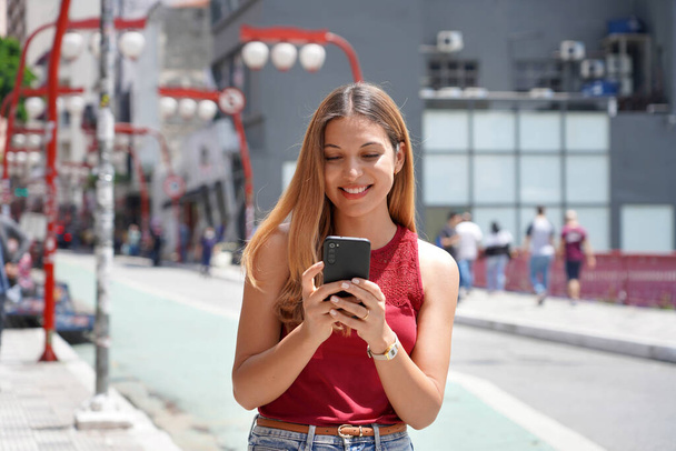 Feliz hermosa adolescente sonriente chateando con su teléfono celular caminando en Sao Paulo, Brasil - Foto, Imagen