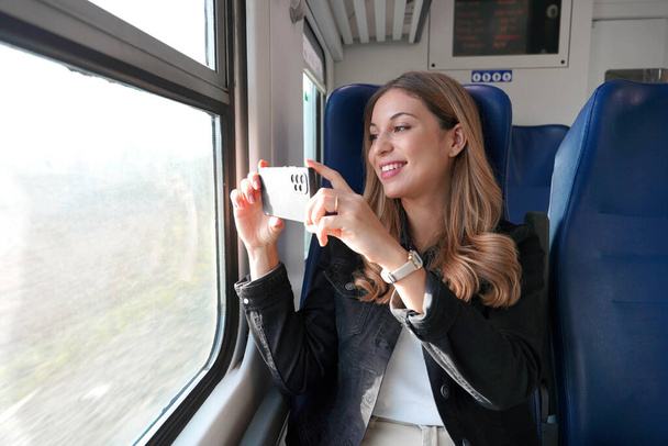 Bella ragazza scatta foto di paesaggio con il suo smartphone seduto sul treno - Foto, immagini