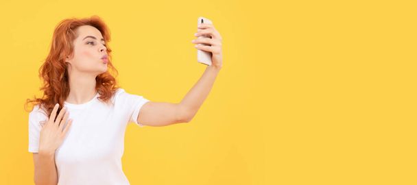 Nainen puhaltaa ilmaa suudelma ottaen selfie kameran puhelimen keltainen tausta, omakuva kuva. Nainen eristetty kasvot muotokuva, banneri mallintaa kopioi tilaa - Valokuva, kuva