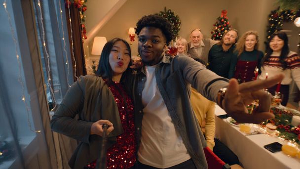 Aasialainen nainen selfie tikku tallentaa videon tai ottaa kuvia perheen kanssa. Monikulttuurinen perhe juhlii joulua tai uutta vuotta. Perhejouluillallisen ilmapiiri kotona. Kamera näkymä. - Valokuva, kuva