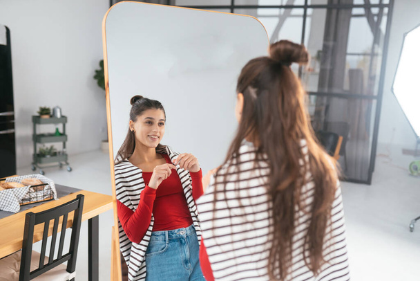 Happy young woman applies makeup on her face in front of the mirror - Photo, Image