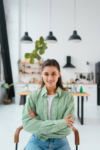 Portrait of a beautiful woman sitting on a chair in a modern kitchen on the background - Photo, image