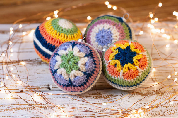 crocheted decorations for the Christmas tree. Bright balls with different crochet pattern of colored lace. White wooden background and led lights - Foto, immagini