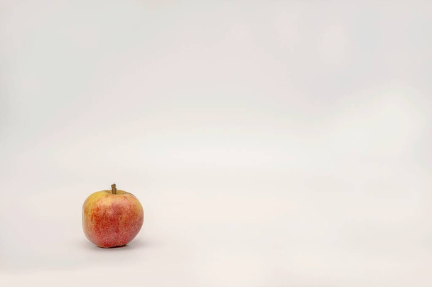 Yksi punainen kypsä omena tuoreesta maatilan sadosta sijaitsee suuren valkoisen bannerin taustan nurkassa. Studio valokuvaus terveellisiä hedelmiä. - Valokuva, kuva