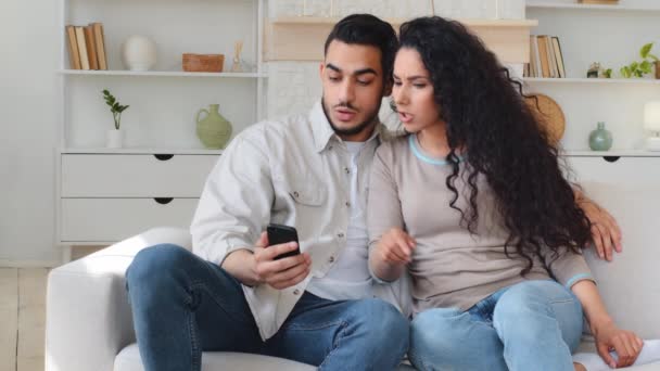 Hispánský indický kavkazský mezirasový multietnický ženatý pár muž manžel přítel a žena manželka přítelkyně na gauči při pohledu na mobilní telefon vybrat zboží on-line hádka diskutovat konflikt - Záběry, video