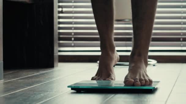 Zbliżenie męskie nogi stóp stojących na elektronicznej wagi kontroli wagi. Sportowe nierozpoznawalne facet człowiek sportowiec boso kontroli ciała kilogramy sprawdzić wyniki treningu sportowego i zdrowego odżywiania - Materiał filmowy, wideo