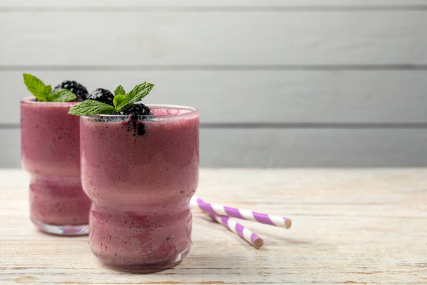 Glasses of blackberry smoothie with mint and berries on light wooden table,. Space for text - Foto, Imagen