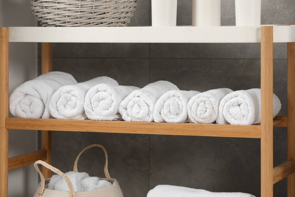 Wooden shelf and wicker basket with soft terry towels in bathroom - Foto, Bild