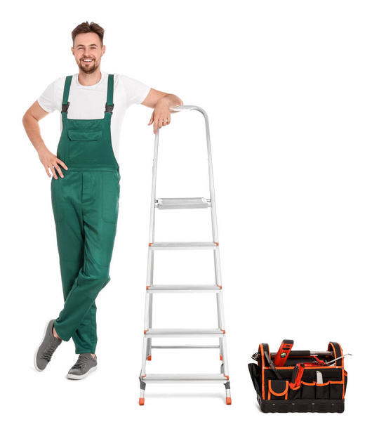 Worker in uniform near metal ladder on white background - Valokuva, kuva