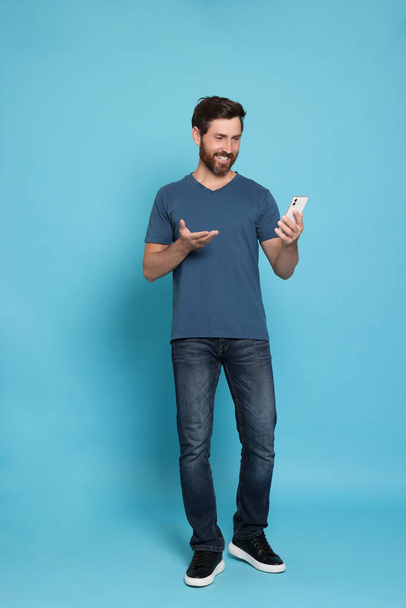 Handsome man having video chat on phone against light blue background - Photo, image
