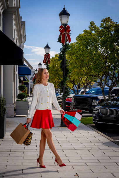 Una hermosa modelo rubia disfruta de un día cálido durante la temporada navideña para hacer algunas compras locales. - Foto, imagen