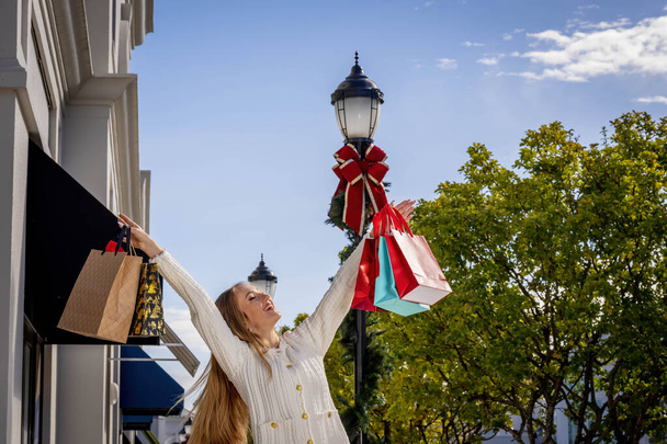 Een prachtig blond model geniet van een warme dag tijdens de kerstvakantie om wat lokale boodschappen te doen - Foto, afbeelding