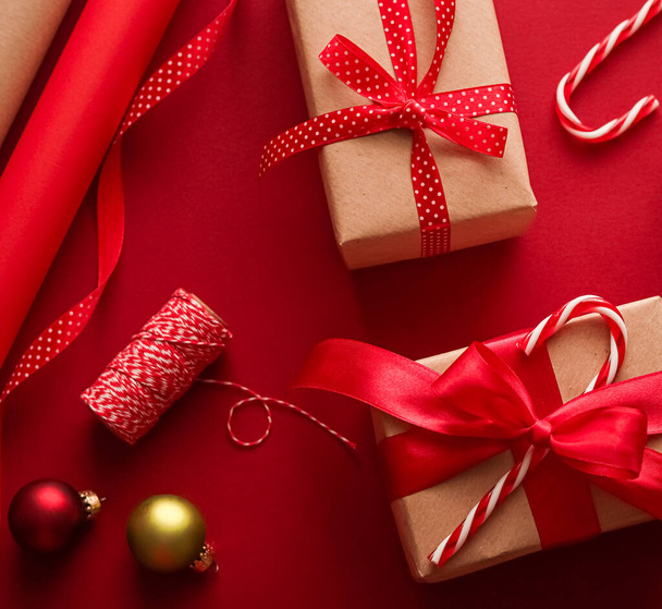 Χριστουγεννιάτικη προετοιμασία, την ημέρα πυγμαχίας και τις γιορτές δώρο δίνοντας, χριστουγεννιάτικο χαρτί χειροτεχνίας και κορδέλες για τα δώρα κουτιά σε κόκκινο φόντο ως εργαλεία περιτύλιξης και διακοσμήσεις, diy παρουσιάζει ως διακοπές επίπεδη lay σχεδιασμό - Φωτογραφία, εικόνα