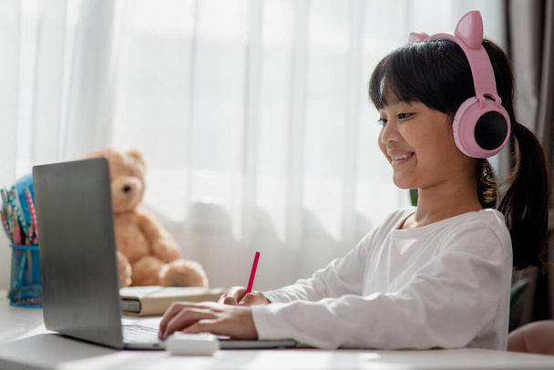 Asiática niña en los auriculares tienen videollamada clase distante con el profesor utilizando el ordenador portátil, estudio en línea en el ordenador, concepto de educación en casa - Foto, imagen