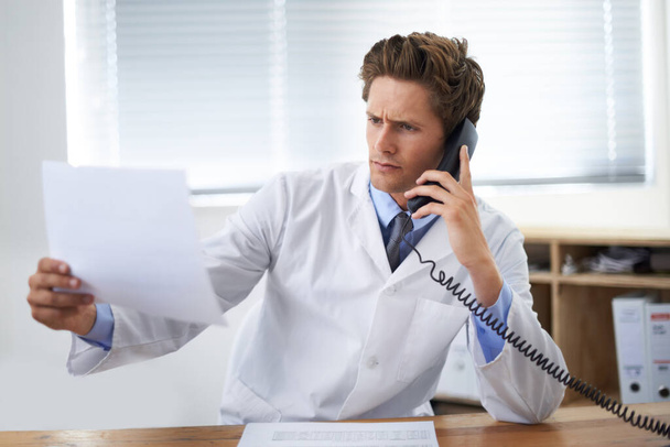 Deze resultaten kunnen niet correct zijn. een bezorgde arts die in zijn kantoor zit en aan de telefoon praat terwijl hij het papierwerk bekijkt - Foto, afbeelding