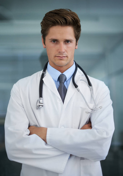 あなたの健康について真剣に。腕を組んで立っている真剣な表情の若い医師の肖像画が折り畳まれて - 写真・画像
