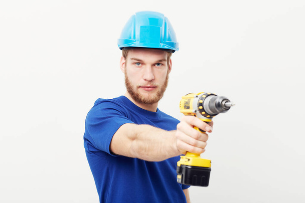 Maak optimaal gebruik van elektrisch gereedschap. Portret van een serieus uitziende jongeman met een helm en een boormachine. - Foto, afbeelding