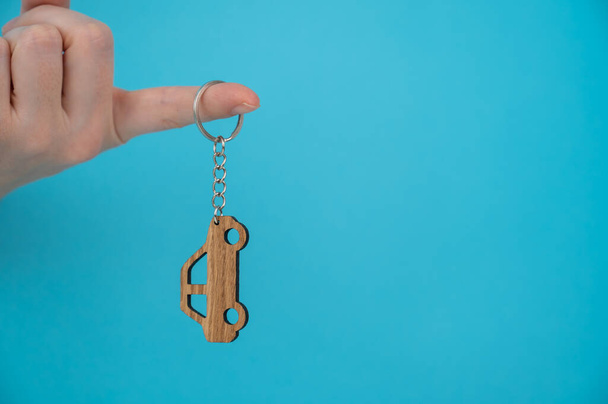 Womans hand holding a wooden keychain in the shape of a car on a blue background - Foto, Bild