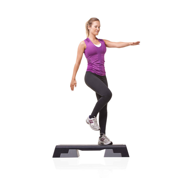 Stepping up her fitness levels. A smiling young woman doing aerobics on an aerobic step against a white background - Photo, Image