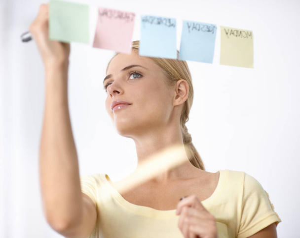 Tijdmanagement is de sleutel. Een mooie jonge vrouw schrijft op post-its geplakt aan een glazen muur - Foto, afbeelding