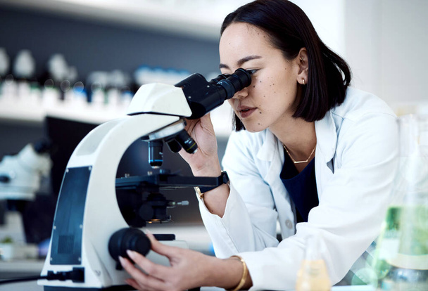 Microscope, Asian woman and in laboratory for research, innovation and science method for healthcare. Female researcher, lady and medical professional with lab equipment, check sample and results - Photo, image