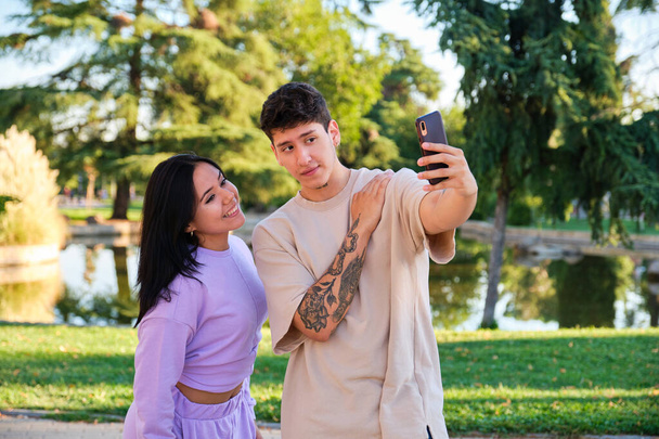 Dwoje młodych Latynosów robi sobie selfie ze smartfonem i uśmiecha się na ulicy w parku. - Zdjęcie, obraz