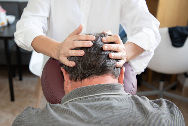 Masážní terapeut muž masíruje mužskou lebku sedící na masáži sedící žena specialista na kolenní masážní křeslo - Fotografie, Obrázek