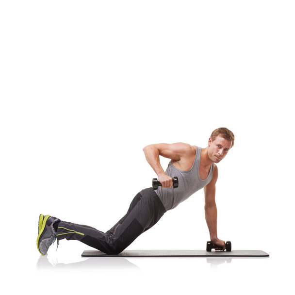 Doing the row technique. A fit young man performing the row exercise with dumbbells on a mat - Photo, image