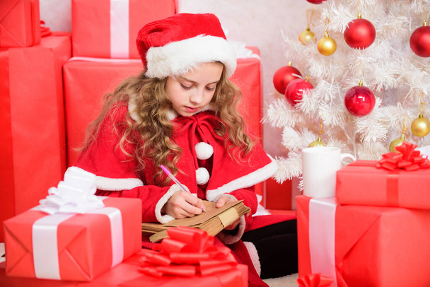 I was good girl all year. Child write letter to santa claus. Child santa costume believe in miracle. Letter for santa. Wish list. Girl little kid hold pen and paper near christmas tree writing letter. - Valokuva, kuva