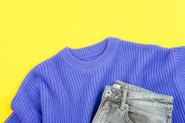 Lila Pullover und graue Jeans auf gelbem Hintergrund. Lässiges Frauen-Outfit. Draufsicht, flache Lage. - Foto, Bild