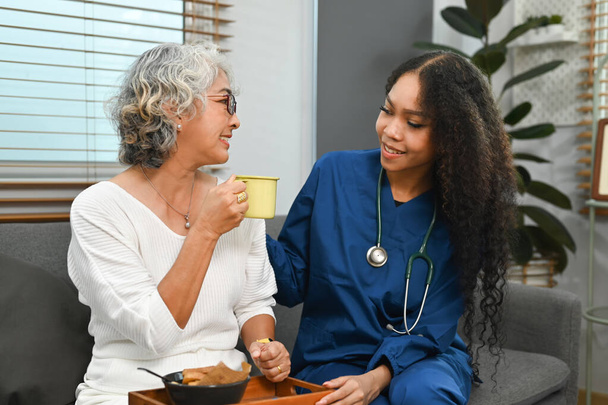 Positive female health visitor talking, giving advice to elderly woman during home visit. Elderly healthcare concept. - Foto, Imagem