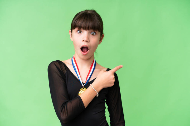 Petite fille caucasienne avec des médailles sur fond isolé surpris et pointant côté - Photo, image