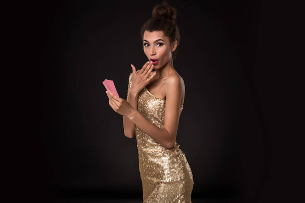 Woman winning - Young woman in a classy gold dress holding two cards, a poker of aces card combination. Studio shot on black background. Emotions - Photo, Image