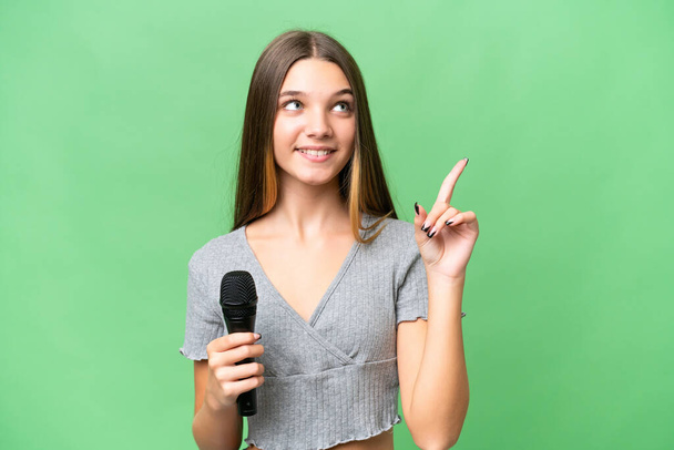 Genç şarkıcı kız izole edilmiş bir arka planda mikrofonu eline aldı ve harika bir fikri işaret etti. - Fotoğraf, Görsel
