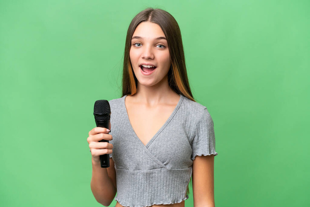 Adolescente cantora menina pegar um microfone sobre fundo isolado com expressão facial surpresa - Foto, Imagem
