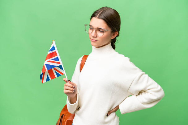 Teenager student caucasian girl holding an United Kingdom flag over isolated background suffering from backache for having made an effort - Фото, изображение