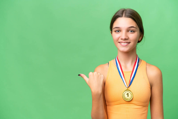 Adolescente caucasienne avec des médailles sur fond isolé pointant vers le côté pour présenter un produit - Photo, image