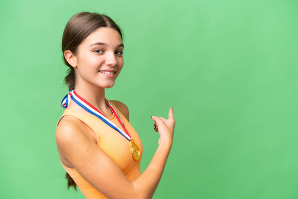 Adolescente chica caucásica con medallas sobre fondo aislado apuntando hacia atrás - Foto, Imagen