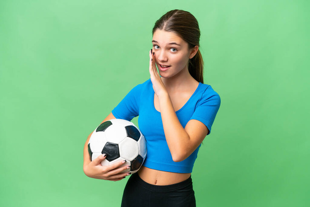 Teenager caucasian girl playing football over isolated background whispering something - Photo, Image