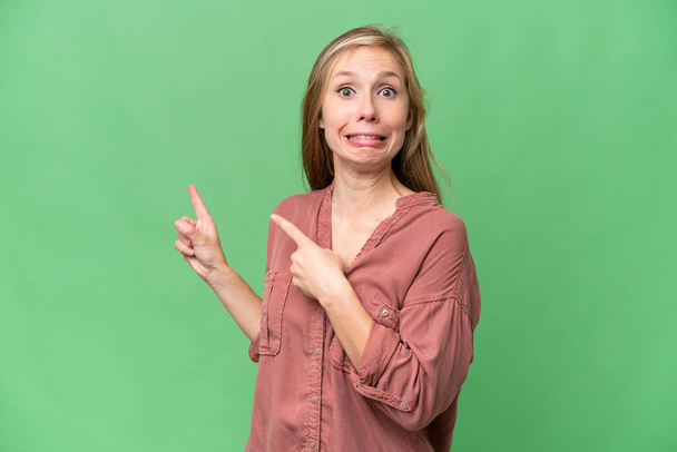 Young blonde woman over isolated background frightened and pointing to the side - Foto, Bild