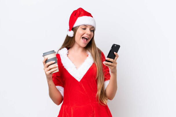 Anne Noel gibi giyinmiş genç beyaz bir kadın beyaz arka planda izole edilmiş. Elinde kahve ve bir cep telefonu var. - Fotoğraf, Görsel