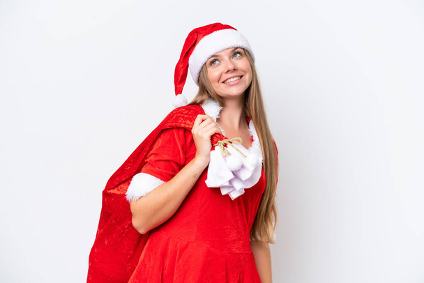 Anne Noel gibi giyinmiş, beyaz arka planda izole edilmiş Noel çuvalını tutan beyaz bir kadın gülümserken yukarı bakıyor. - Fotoğraf, Görsel