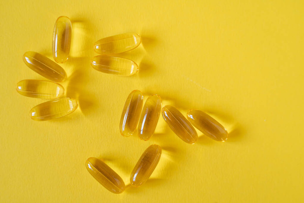 Transparent gel fish oil capsules with omega-3 and vitamin D isolated on yellow background. Food supplements and vitamins. Healthy diet and skin treatment concept. - Fotografie, Obrázek