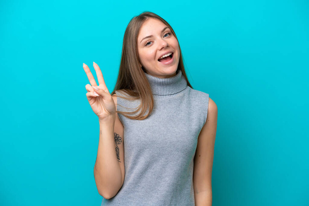 Young Lithuanian woman isolated on blue background smiling and showing victory sign - Zdjęcie, obraz