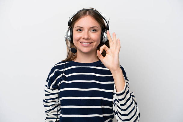 Telemarketer mujer caucásica trabajando con un auricular aislado sobre fondo blanco mostrando signo de ok con los dedos - Foto, imagen