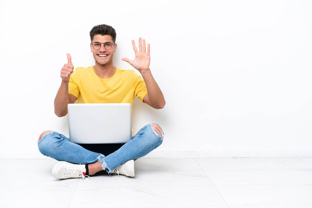 Young man sitting on the floor isolated on white background counting six with fingers - Φωτογραφία, εικόνα